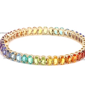 May include: A gold bracelet with a rainbow of oval-shaped gemstones. The bracelet is made of 14k gold and features a total of 2.5 carats of gemstones. The gemstones are set in a pave setting and are arranged in a rainbow pattern. The bracelet is approximately 7 inches in length.