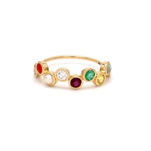 May include: A gold ring with a row of colorful gemstones, including red, white, green, and yellow. The ring is set with a variety of stones, including a diamond, ruby, emerald, and sapphire.