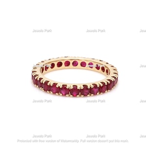 May include: A gold band ring with a row of small, round, red ruby stones set in the band.