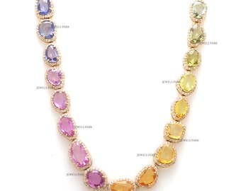 May include: A gold necklace with a rainbow of gemstones. The necklace features oval-shaped gemstones in shades of blue, purple, pink, orange, yellow, and green. Each gemstone is surrounded by a halo of smaller diamonds.