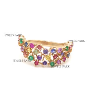 Puede incluir: Un anillo de oro con un racimo de piedras preciosas de colores. El anillo está engastado con una variedad de pequeñas piedras redondas en tonos rojos, azules, verdes, amarillos y morados.