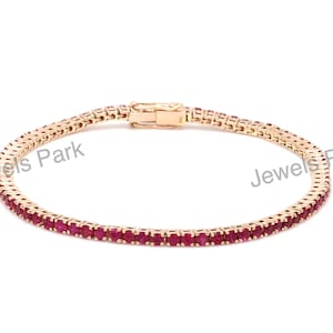 May include: A gold tennis bracelet with a row of red ruby stones.