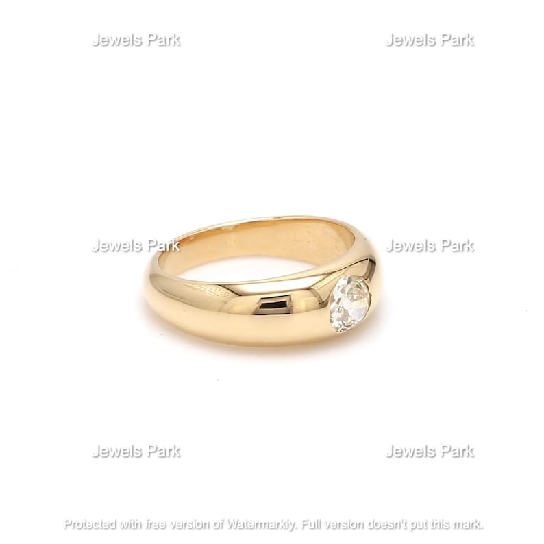 May include: A gold ring with a single round, clear gemstone set in the center. The ring has a smooth, rounded band.