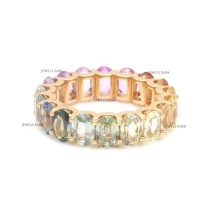 May include: A gold band ring with a rainbow of oval-shaped sapphires. The ring is set with a row of sapphires in shades of blue, green, yellow, and pink.