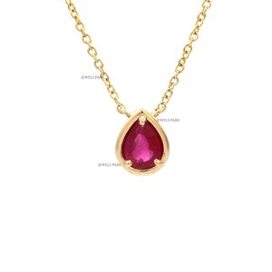 May include: A gold-colored necklace with a teardrop-shaped, ruby-colored pendant. The pendant is set in a gold bezel and hangs from a delicate gold chain. The text "JEWELS PARK" is visible on the image.