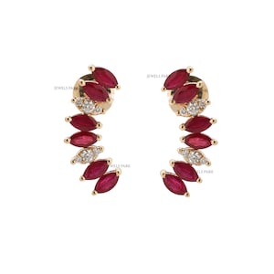 Puede incluir: Un par de pendientes dorados con un diseño curvo. Cada pendiente presenta piedras preciosas rojas oscuras con corte marquesa y pequeños diamantes blancos brillantes. El texto "JEWELS PARK" es visible.