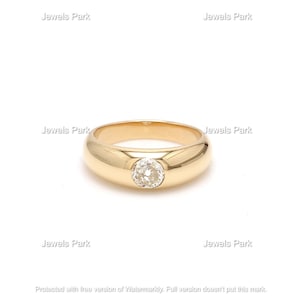 May include: A gold ring with a round, clear gemstone set in the center. The ring has a thick band.