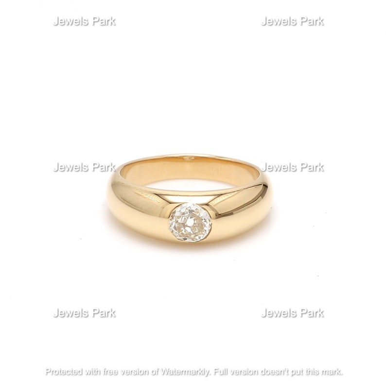 May include: A gold ring with a round, clear gemstone set in the center. The ring has a thick band.