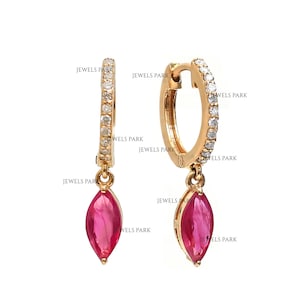 May include: Gold hoop earrings with a dangling ruby marquise-shaped gemstone. The hoop is accented with small diamonds.