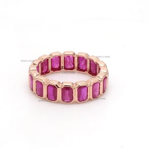 May include: A rose gold band ring with a row of emerald-cut pink gemstones. The ring is set with a total of 14 gemstones.