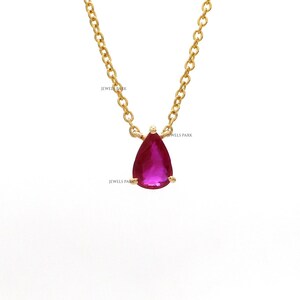May include: A gold-colored chain necklace with a pear-shaped, deep pink gemstone pendant. The pendant is suspended from a delicate chain. The words "JEWELS PARK" are printed on the image.