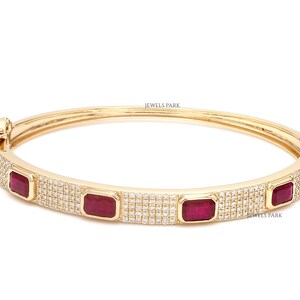 May include: Gold bangle bracelet featuring rectangular red gemstones and small white stones. The bracelet has a hinged clasp and the text "JEWELS PARK". This elegant piece of jewellery is suitable for special occasions.