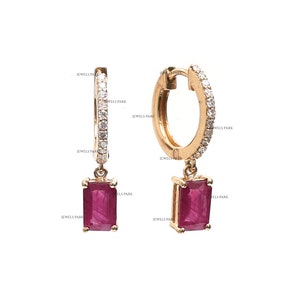 May include: A pair of gold hoop earrings with a dangling red gemstone. The hoops are accented with small diamonds.