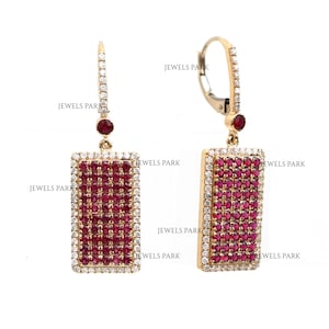May include: Gold-tone rectangular drop earrings. Each earring features a rectangular cluster of small, deep red gemstones surrounded by a border of smaller, clear gemstones. A small red gemstone and clear gemstones accent the top of each earring.