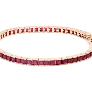 Pode incluir: Uma pulseira de ouro com uma fileira de rubis vermelhos quadrados. A pulseira é feita de uma fina banda de metal com um fecho lateral. "Jewels Park" está impresso na pulseira.