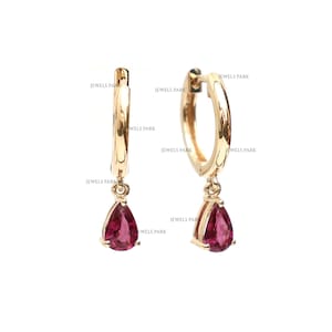 May include: A pair of gold hoop earrings with a dangling pear-shaped pink gemstone.