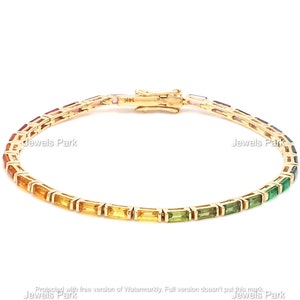 May include: A gold bracelet with a rainbow of rectangular gemstones. The bracelet has a secure clasp and is marked "14K". The gemstones transition from red to orange, yellow, green, and blue. The brand name "Jewels Park" is visible.