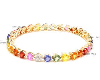 Puede incluir: Un brazalete de oro con un arcoíris de zafiros en forma de corazón y un solo diamante. El brazalete está hecho de oro de 14 quilates y presenta un total de 2,5 quilates de zafiros.