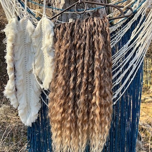 May include: A set of long, curly ombre hair extensions in shades of brown and blonde. The extensions are hanging from a hanger and are surrounded by blue and white string.