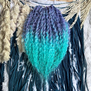 Puede incluir: Un conjunto de rastas sintéticas rizadas de color azul y verde degradado. Las rastas están dispuestas en forma de abanico y están listas para ser instaladas.