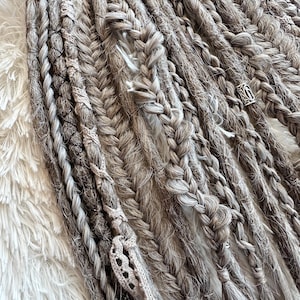 May include: A set of gray and white synthetic dreadlocks with a silver bead accent. The dreadlocks are made of a variety of textures, including braids, twists, and crochet.