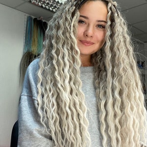 May include: A woman with long, wavy, light blonde hair. She is wearing a gray sweatshirt.