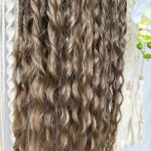 May include: Close-up of long, wavy brown hair extensions. The hair has a mix of light and dark brown tones, creating a natural look. The curls are tightly wound and cascade down. The extensions are likely for adding length or volume.