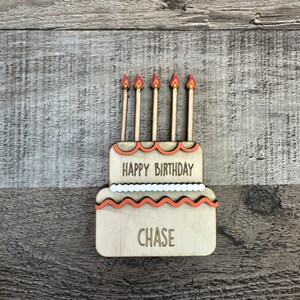 May include: Wooden birthday cake with five orange candles and the text "Happy Birthday Chase" on it.