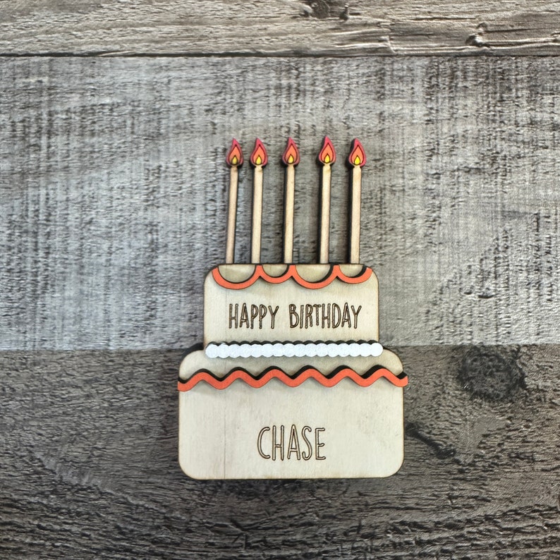 May include: Wooden birthday cake with five orange candles and the text "Happy Birthday Chase" on it.