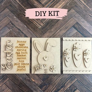 以下が含まれることがあります： 3つの木製パネルを使用したDIYイースタークラフトキット。最初のパネルには、「イースター」という言葉が縦書きで書かれており、イースターをテーマにした単語のリストがあります。2番目のパネルには、バナーに「ホップ」という言葉が書かれたウサギのシルエットがあります。3番目のパネルには、ハートと花が付いたニンジンが3本あります。