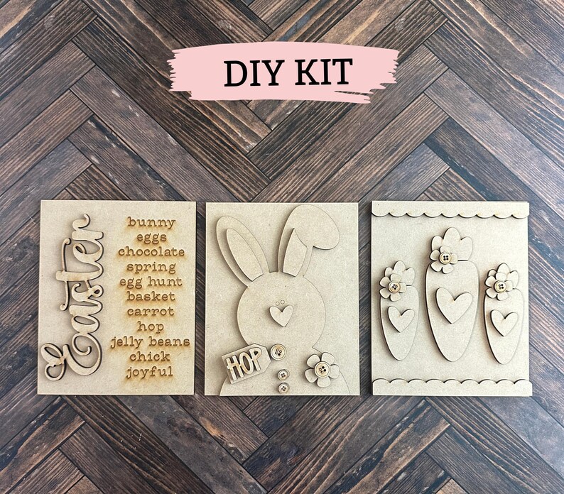 以下が含まれることがあります： 3つの木製パネルを使用したDIYイースタークラフトキット。最初のパネルには、「イースター」という言葉が縦書きで書かれており、イースターをテーマにした単語のリストがあります。2番目のパネルには、バナーに「ホップ」という言葉が書かれたウサギのシルエットがあります。3番目のパネルには、ハートと花が付いたニンジンが3本あります。