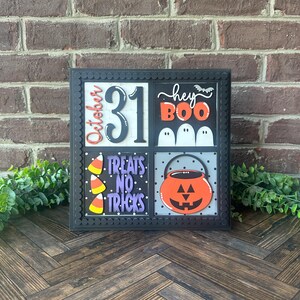 Könnte beinhalten: Ein schwarzes quadratisches Schild mit weißem Hintergrund und verschiedenen Halloween-Dekorationen. Das Schild ist in vier Abschnitte unterteilt. Der obere linke Abschnitt zeigt "October 31". Der obere rechte Abschnitt zeigt "hey boo" mit einer Fledermaus und drei Geistern. Der untere linke Abschnitt zeigt "treats no tricks" mit Mais. Der untere rechte Abschnitt zeigt einen schwarzen Kessel mit einem lächelnden orangefarbenen Kürbisgesicht.