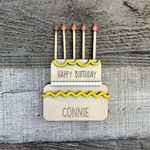 May include: A wooden cake with yellow frosting and five candles. The cake says "Happy Birthday Connie" on it.