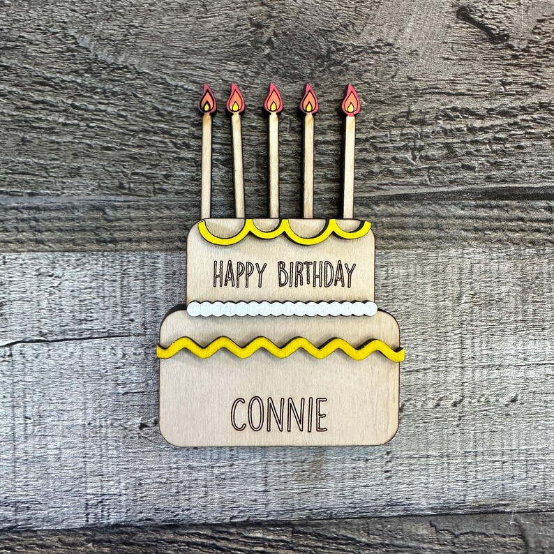 May include: A wooden cake with yellow frosting and five candles. The cake says "Happy Birthday Connie" on it.
