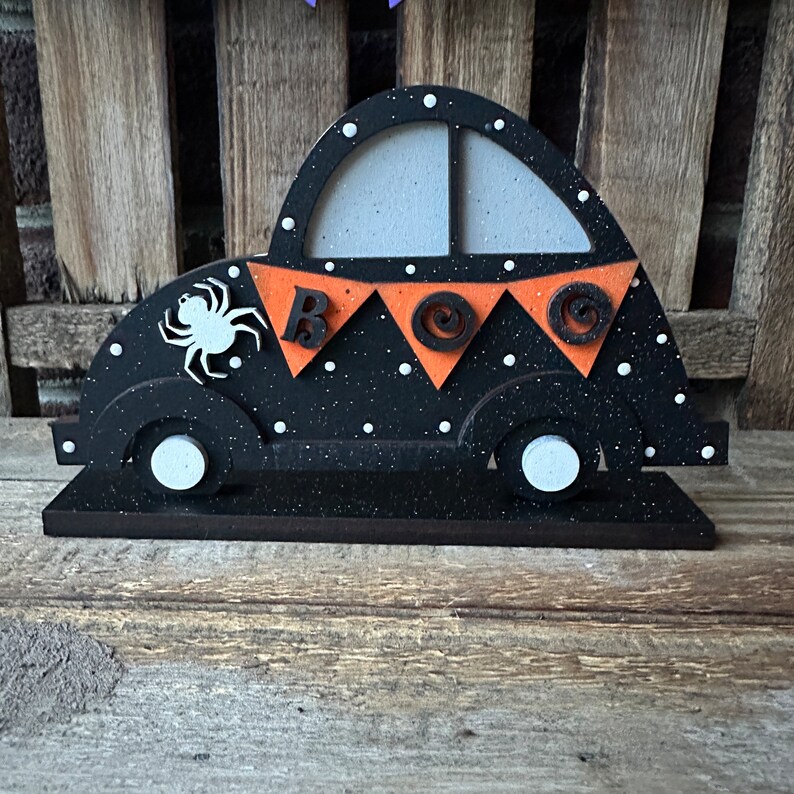 May include: Black wooden car with white polka dots and a spider on the side. The car has orange and black bunting that says "BOO" on it.