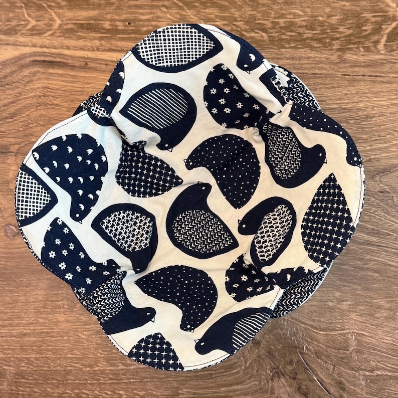May include: A navy blue and cream-colored fabric bowl with a bird pattern. The birds are stylized with various patterns, including dots, cross-hatching, and small floral designs. The bowl is sitting on a wooden surface.