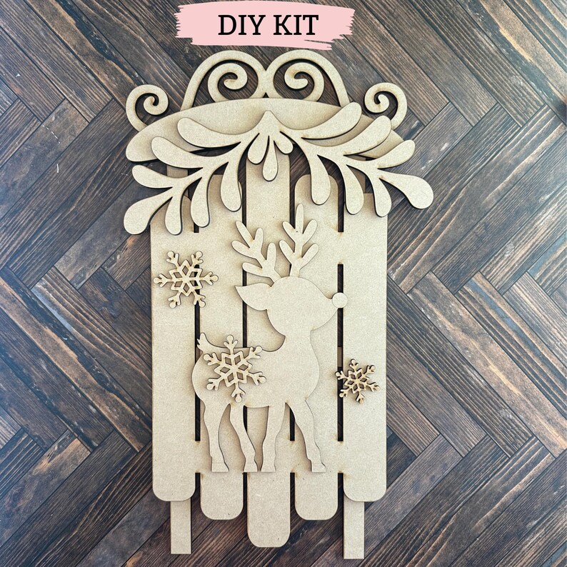 Puede incluir: Kit de bricolaje para una decoraci&oacute;n de trineo de reno navide&ntilde;o de madera. El kit incluye un reno, un trineo, copos de nieve y una guirnalda de hojas.