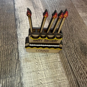 May include: Wooden birthday cake stand with four candles and the words "Happy Birthday Connie" on the front.