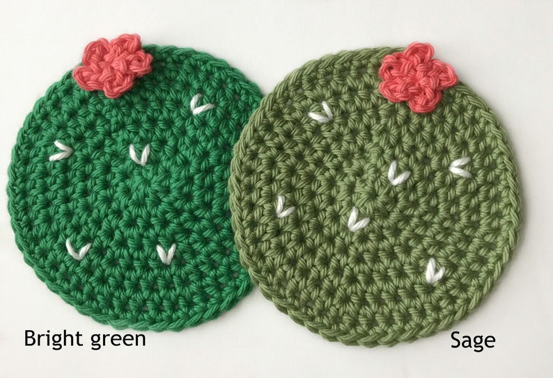 May include: Two crocheted cactus-shaped coasters. One is bright green, the other sage green. Each has a small, coral-colored flower and white stitched details. The text "Bright green" and "Sage" are below the coasters.
