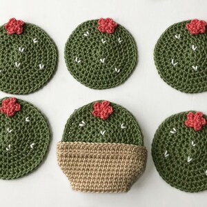 May include: Six handmade crochet cactus coasters. The coasters are round, green, and feature white stitch details and a small red flower. One coaster is in a tan pot. The coasters are designed to protect surfaces from heat and moisture.