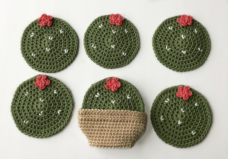 May include: Six handmade crochet cactus coasters. The coasters are round, green, and feature white stitch details and a small red flower. One coaster is in a tan pot. The coasters are designed to protect surfaces from heat and moisture.