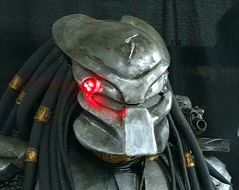 May include: A Predator costume with a detailed, silver and black armored chest piece, a black and brown spear, and a mask with glowing red eyes.