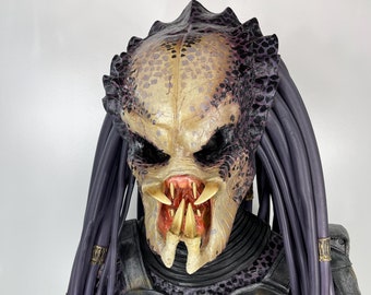 May include: A close-up of a Predator figure with a black and silver armored chest and purple dreadlocks. The figure has a detailed face with sharp teeth and yellow eyes.