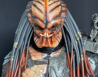 Könnte beinhalten: Ein Predator-Kostüm mit einer detaillierten Maske, schwarzen und roten Dreadlocks und einem silbernen Bruststück.