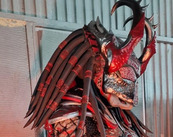 May include: A red and black Predator costume with intricate details, including a helmet with horns and a net-like chest piece.