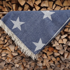 Könnte beinhalten: Eine blaue Wolldecke mit weißen Sternen, mit einem Fransenrand. Die Decke ist über einen Stapel Brennholz gelegt.