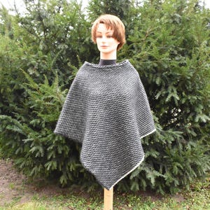 Könnte beinhalten: Ein schwarz-weiß gestricktes Poncho mit weißem Besatz. Das Poncho ist aus einem weichen, strukturierten Stoff gefertigt.