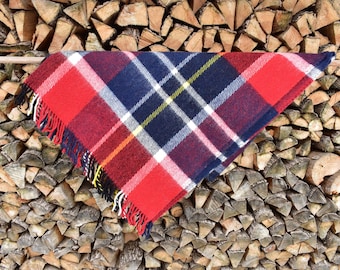 May include: A red, white, blue, and yellow plaid throw blanket with fringe hanging on a wooden fence.