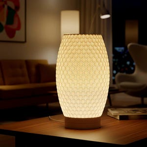 Puede incluir: Una lámpara de mesa crema con un patrón de panal. La lámpara tiene forma cilíndrica y se asienta sobre una base de madera. La lámpara está sobre una mesa de madera oscura en un salón.