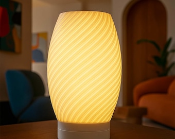 May include: A glowing, egg-shaped table lamp with a white base and a swirling, cream-colored shade. The lamp emits a warm, inviting light, perfect for a living room or bedroom. The lamp is sitting on a dark brown table.